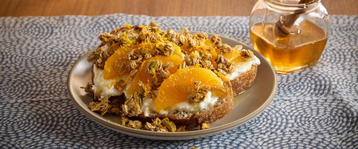 Golden Grove granola on ricotta toast with orange segments, orange zest and a jar of honey