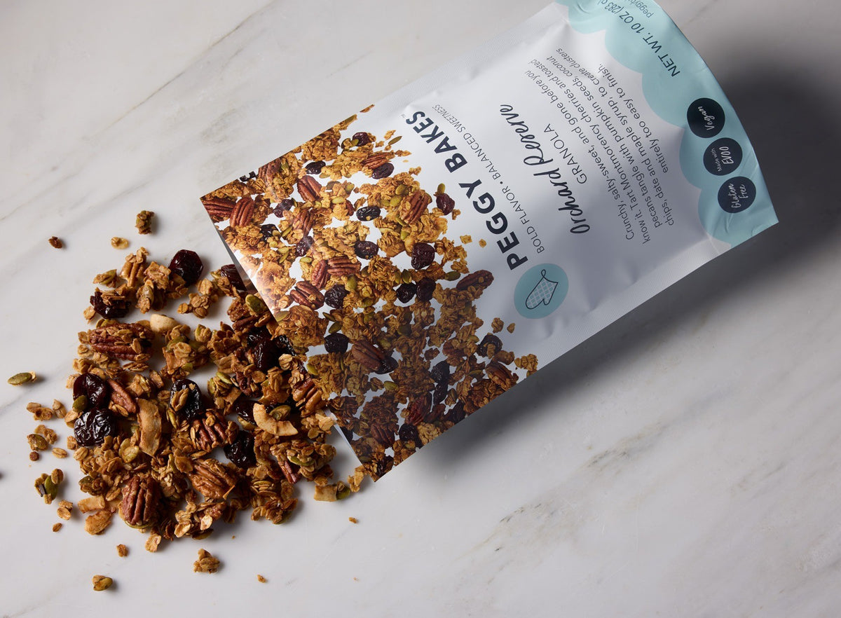 Peggy Bakes Orchard Reserve gluten-free granola spilling from the bag onto white marble